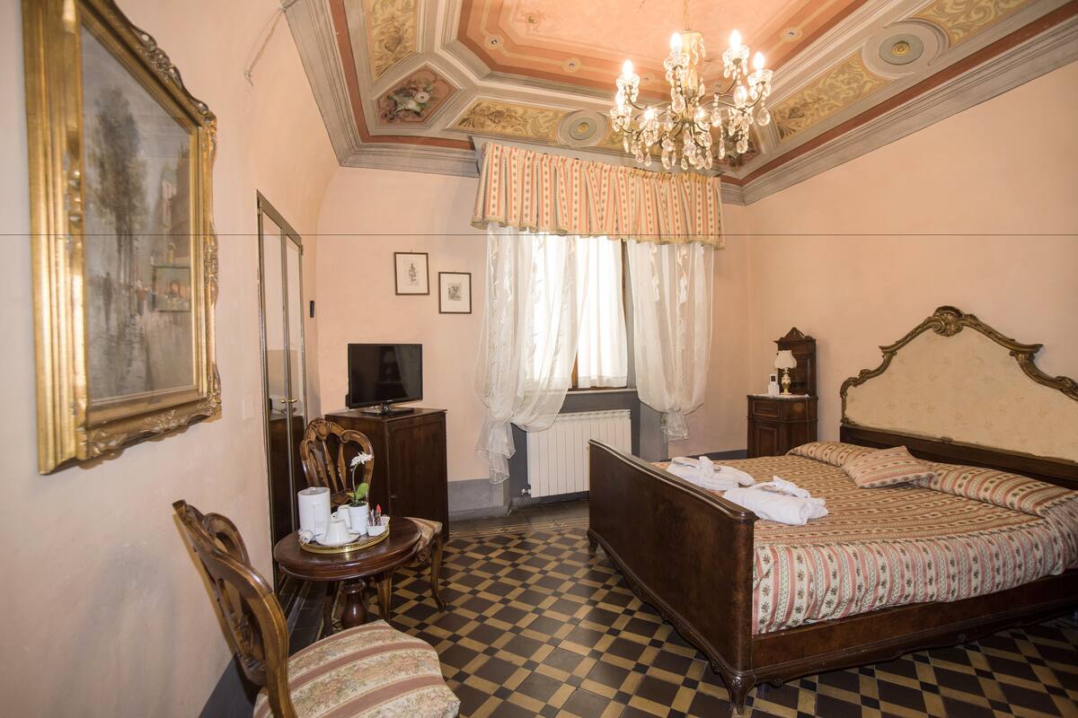 A bedroom with a checkered floor, a large bed, a chandelier, and a mirror.