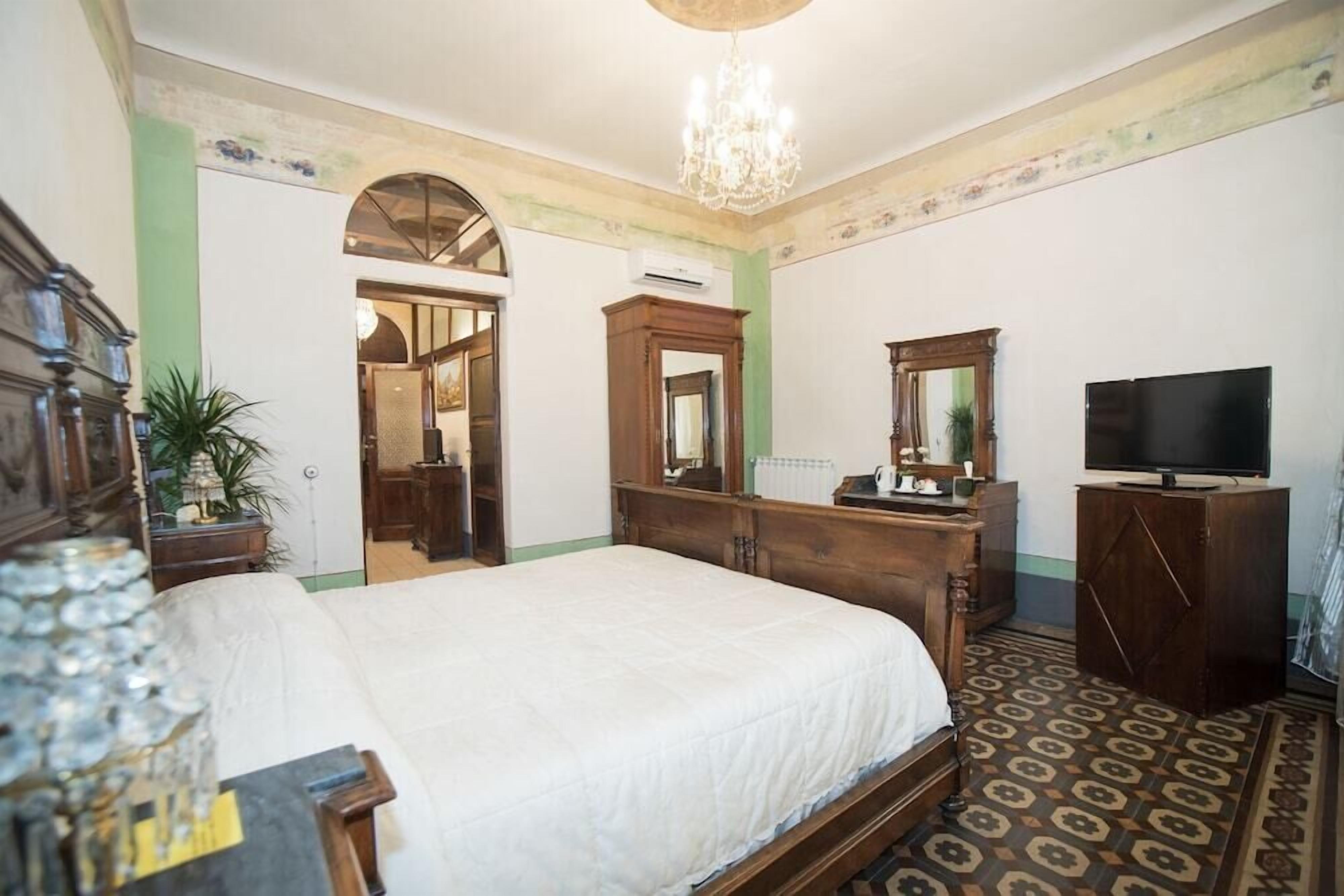 Una habitación de hotel con una cama grande, cómoda de madera, televisor y candelabro.