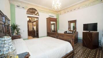 Una habitación de hotel con una cama grande, cómoda de madera, televisor y candelabro.