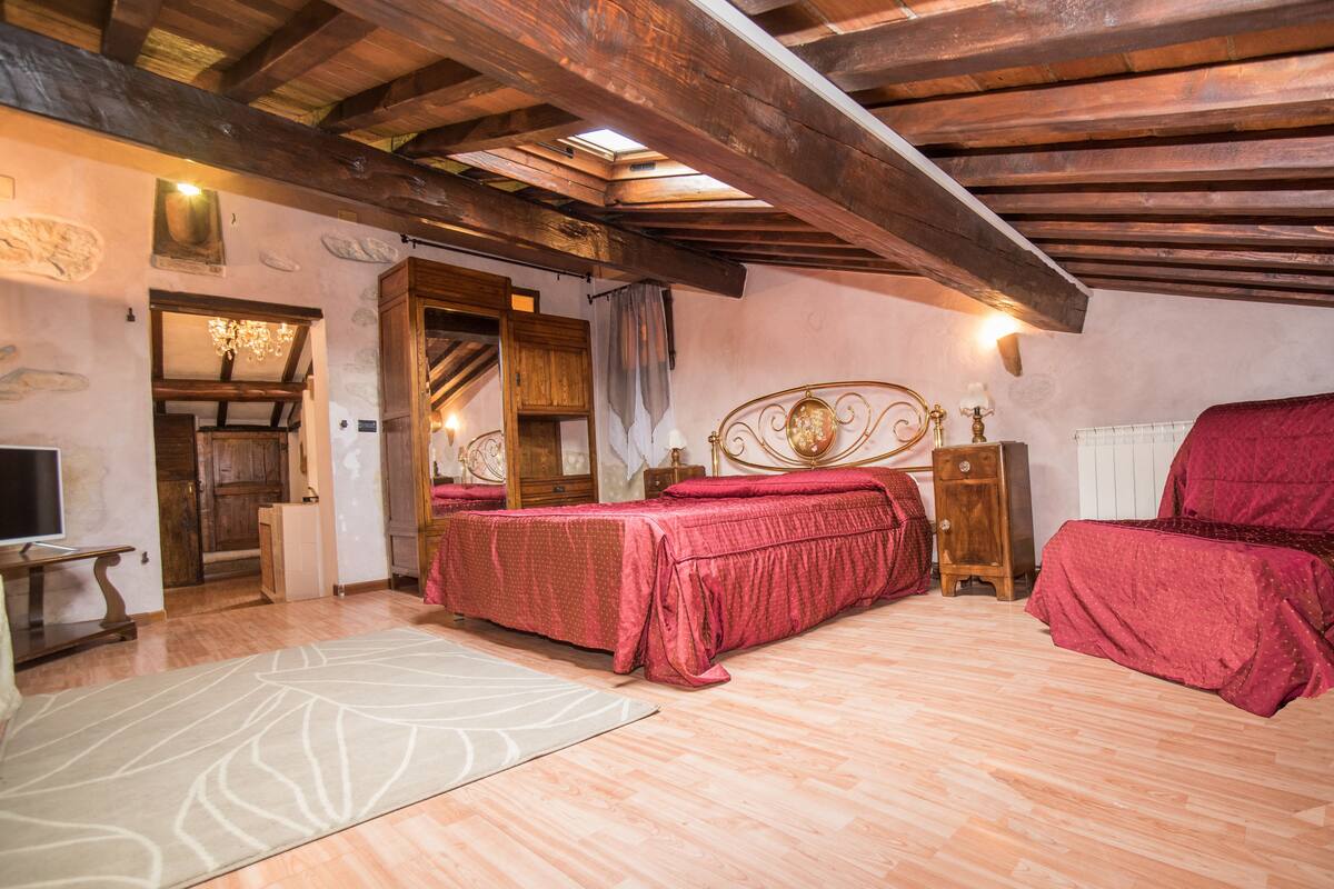 A bedroom with a wooden ceiling, a bed with a red bedspread, a wooden nightstand, and a chair.