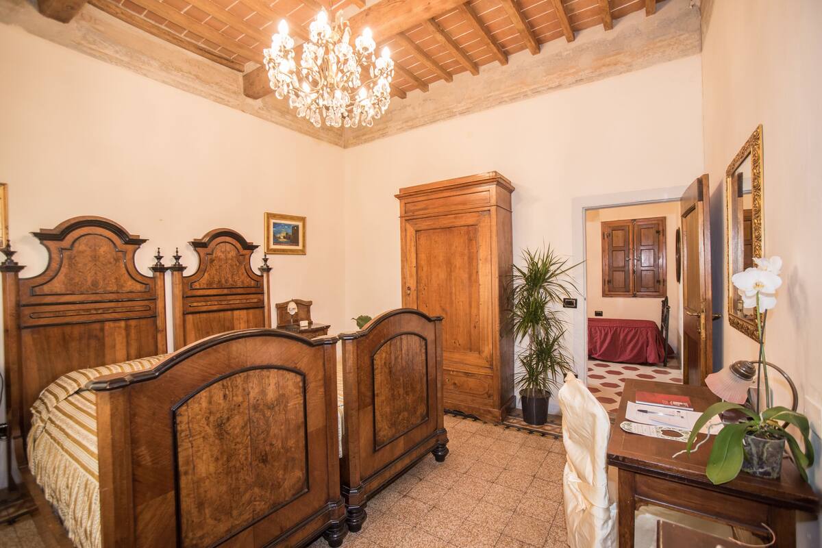 A bedroom with a wooden bed, a desk with a chair, a potted plant, and a chandelier.