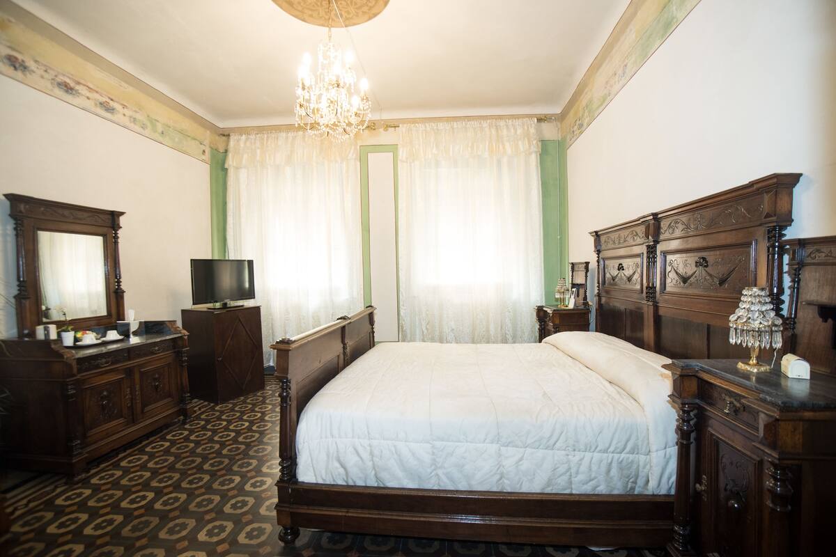A bedroom with a large bed, wooden furniture, a television, and a chandelier.