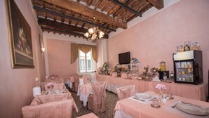 A restaurant with pink tablecloths, wooden beams, and a chandelier. Tables are set with plates, glasses, and flowers. - Relais Centro Storico Pisa (Pisa)