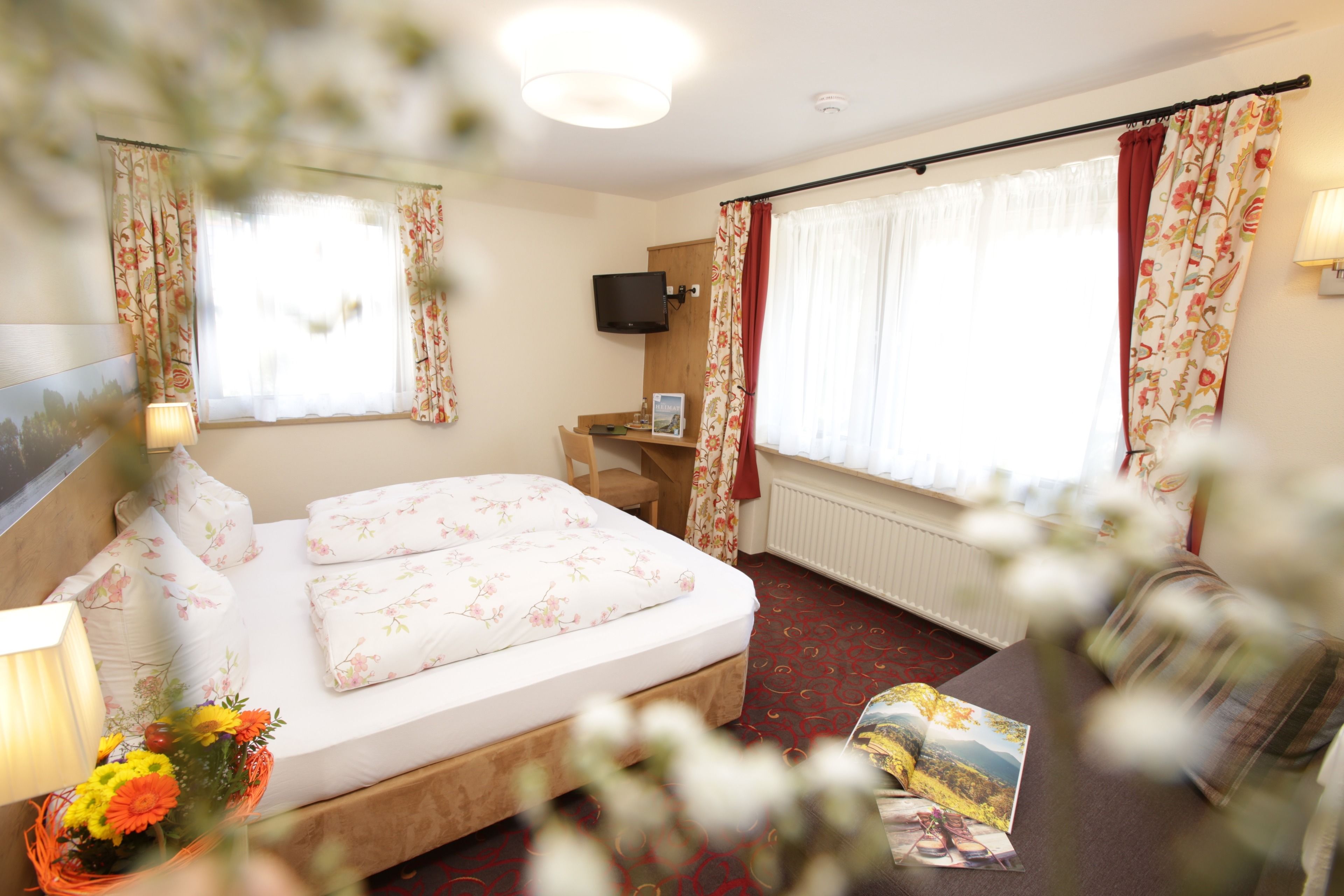 Una habitación de hotel con cama, escritorio, televisor y ventana con cortinas.