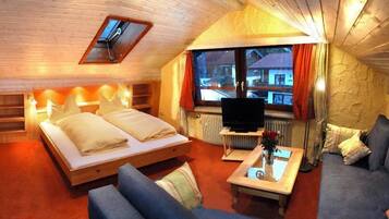 Una habitación acogedora con cama, sofá, televisión y ventana con cortinas.