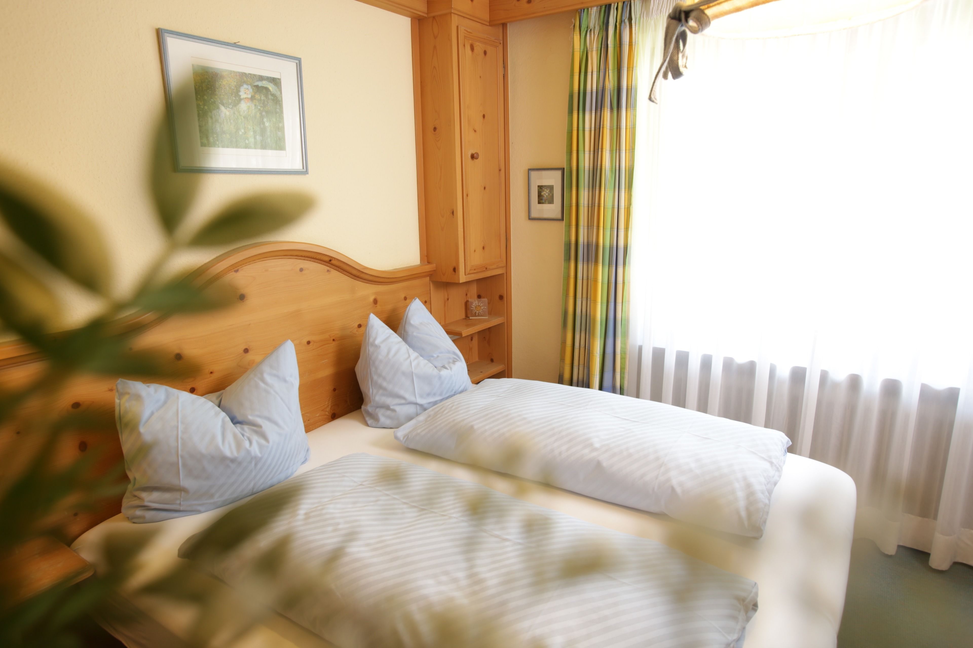 A bedroom with two beds, wooden headboard, a framed picture on the wall, and a window with curtains.