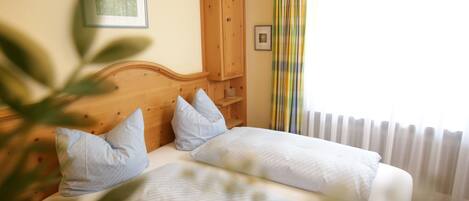 A bedroom with two beds, wooden headboard, a framed picture on the wall, and a window with curtains.