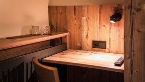 A wooden dining table with a remote control, a wall-mounted light, and two glass containers on a shelf above. - Hotel Garni Landhaus Traunbachhäusl (Ruhpolding)