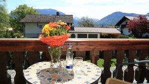 A round table with a mosaic top, a vase with flowers, and a bottle on a balcony overlooking a mountain landscape. - Hotel Garni Landhaus Traunbachhäusl (Ruhpolding)