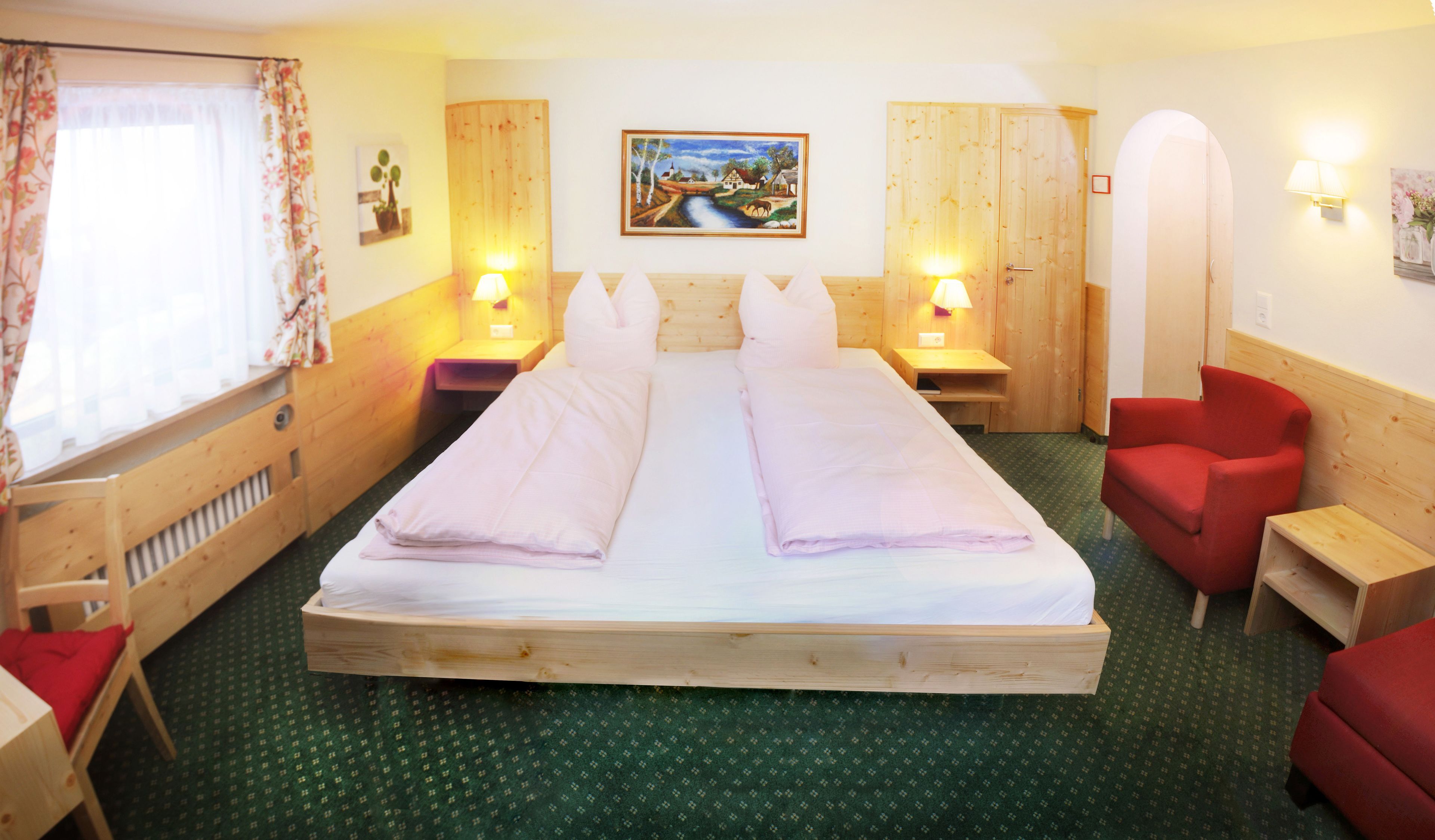 Habitación de hotel con una cama grande, dos mesitas de noche con lámparas, un sillón rojo, un armario de madera y un cuadro en la pared.