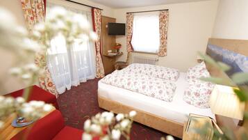 Una camera d'albergo con un letto, una televisione fissata al muro, una finestra con tende e un divano rosso.