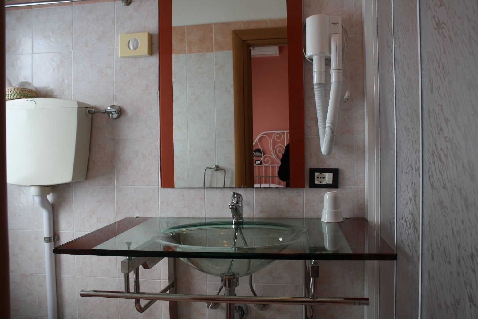 A bathroom with a glass sink, a mirror, a towel rack, and a hairdryer mounted on the wall.