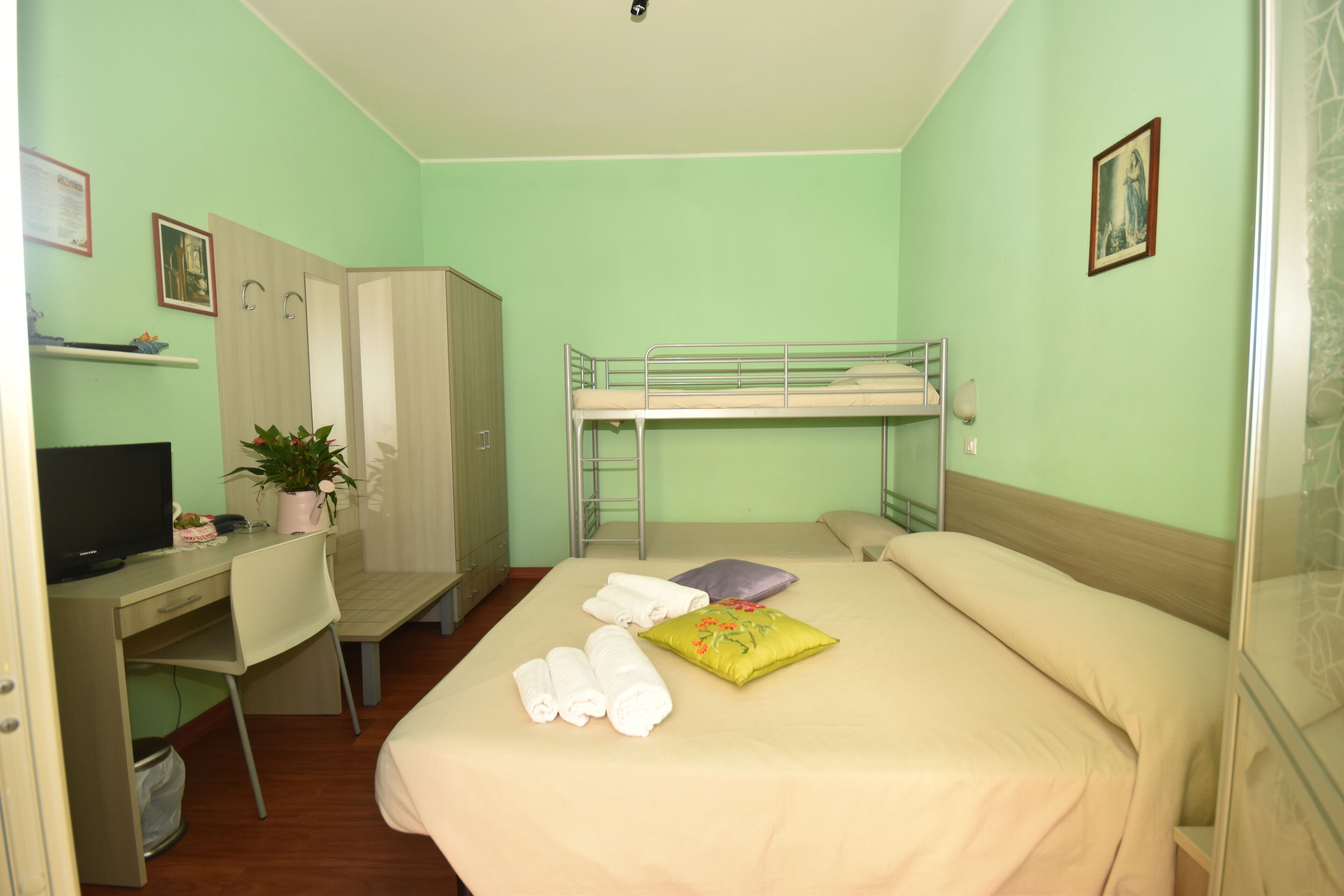 A room with bunk beds, a desk with a computer, a chair, and a bed with towels and pillows.