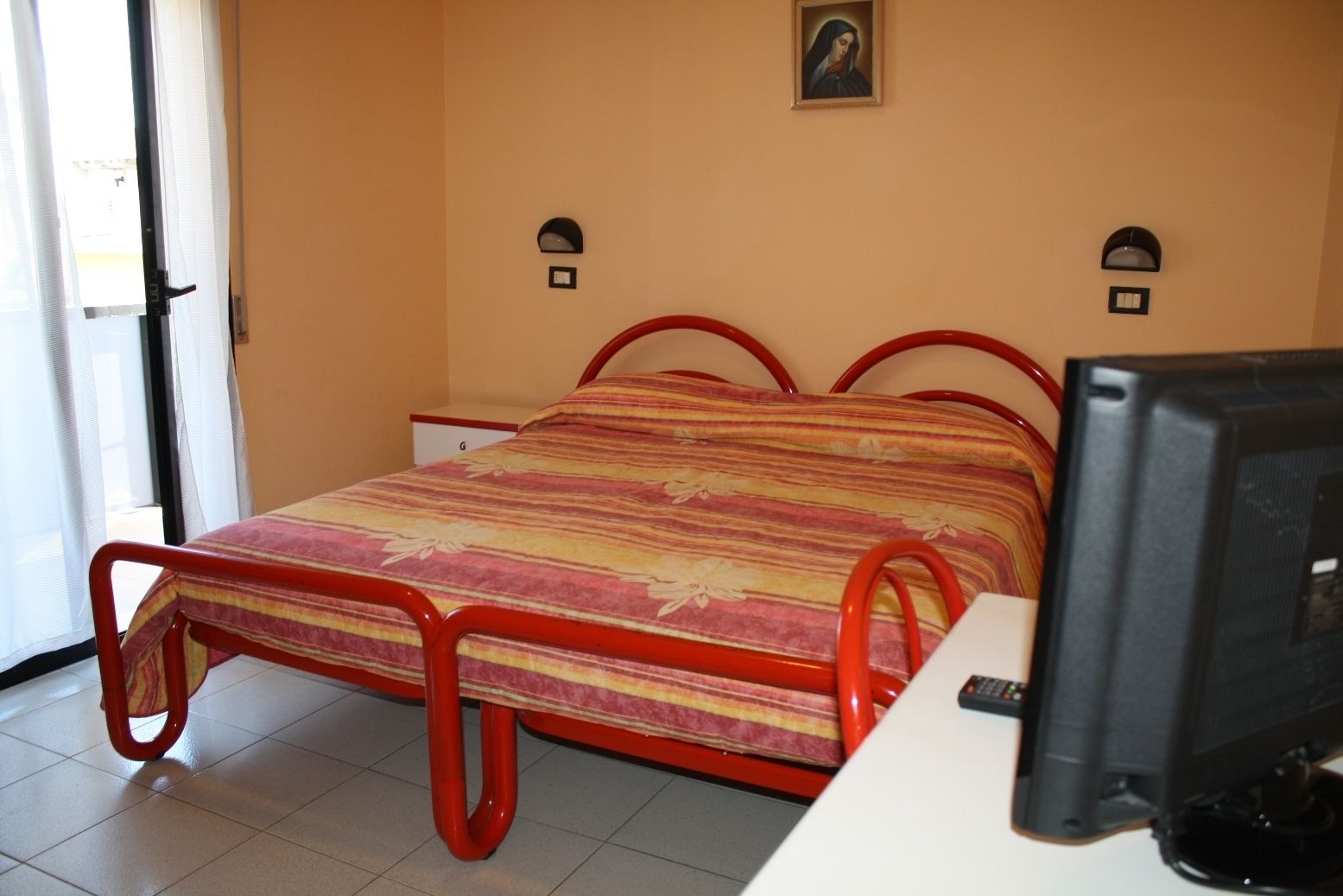 A bedroom with a bed, a desk, a computer, and a window.
