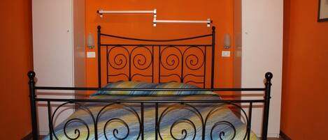 A single bed with a metal frame and a colorful bedspread in a room with orange walls and white cabinets.