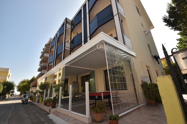 A modern building with a covered entrance, potted plants, and a visible balcony.