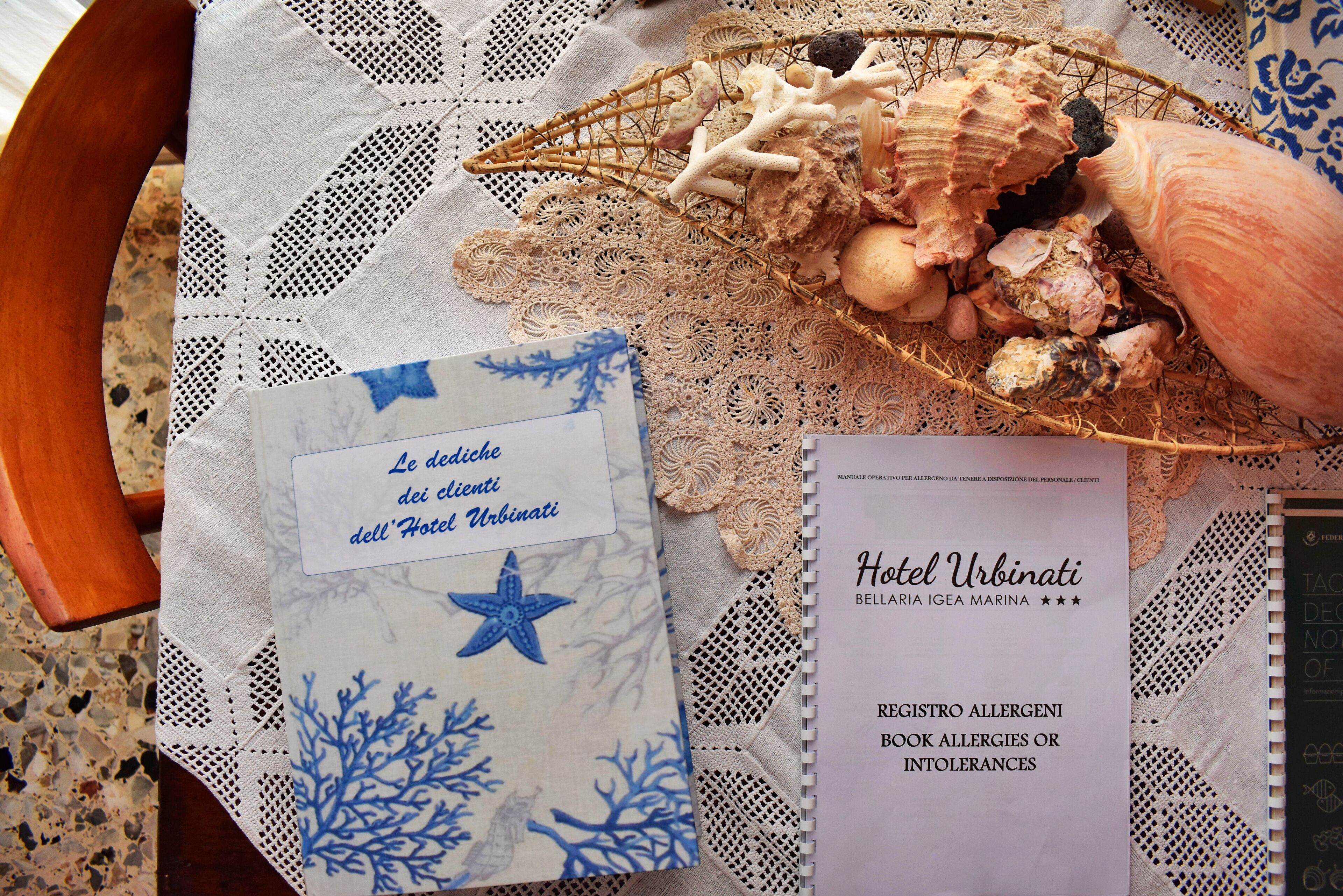A table with a lace tablecloth, a basket of seashells, and a hotel brochure.