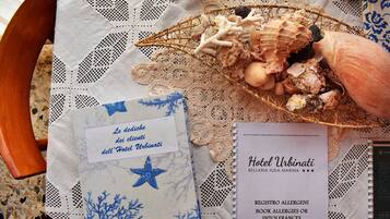 A table with a lace tablecloth, a basket of seashells, and a hotel brochure.