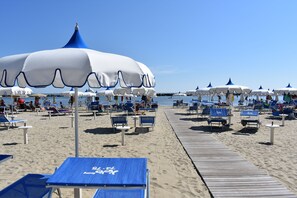 A beach with rows of blue and white beach umbrellas, sun loungers, and a wooden walkway. - Urbinati (Bellaria-Igea Marina)