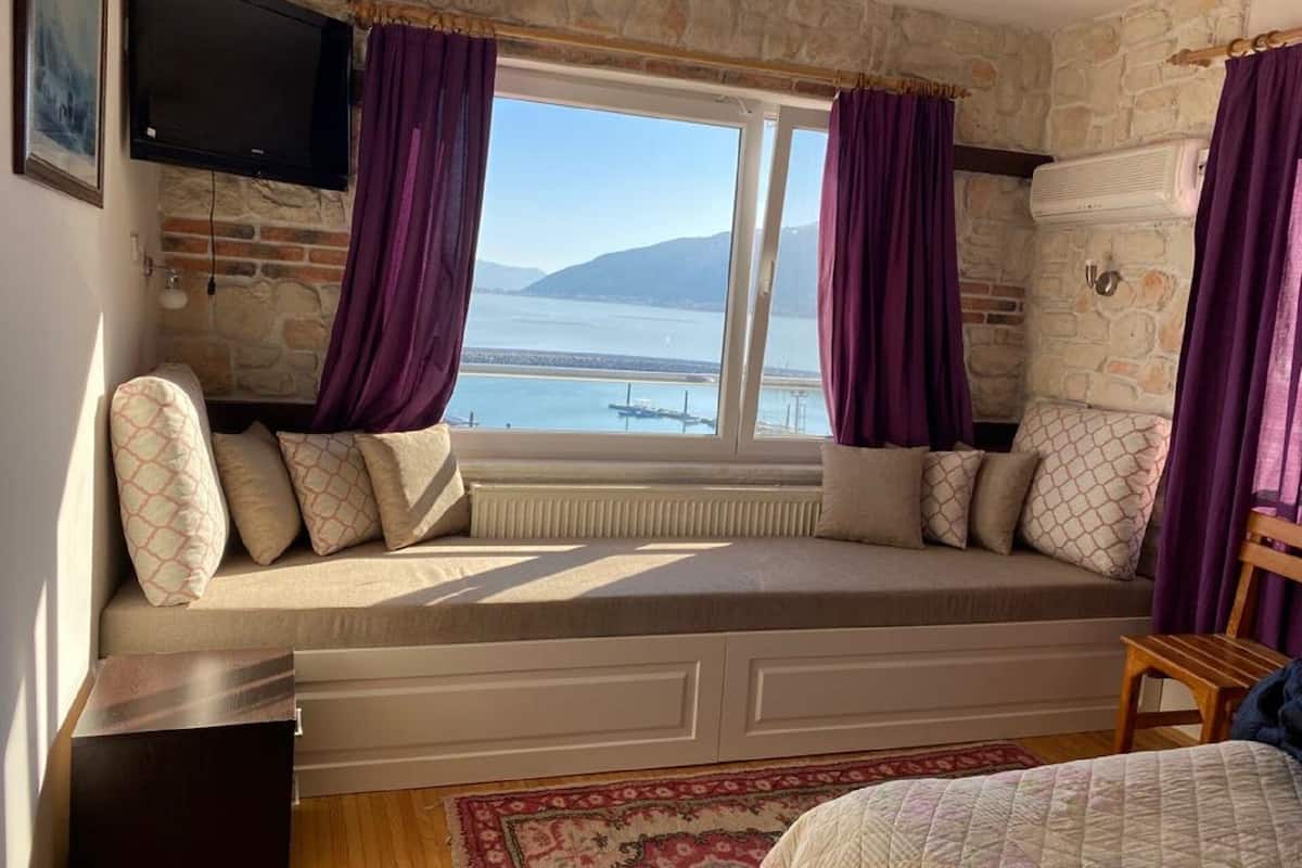 A room with a stone wall, a window with purple curtains, a bed, and a television mounted on the wall.
