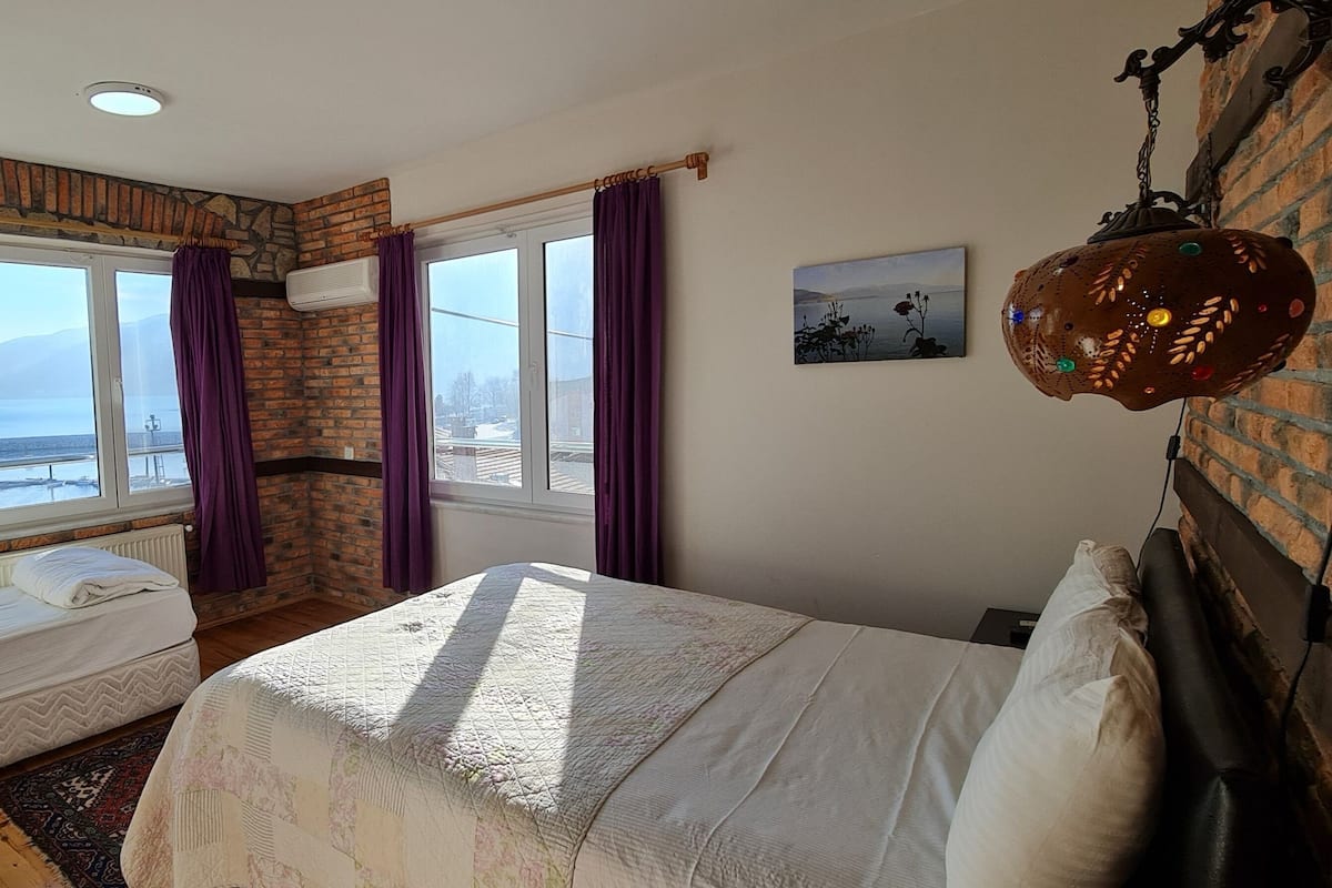 A bedroom with a bed, a window with a view, a TV, and a decorative hanging light.
