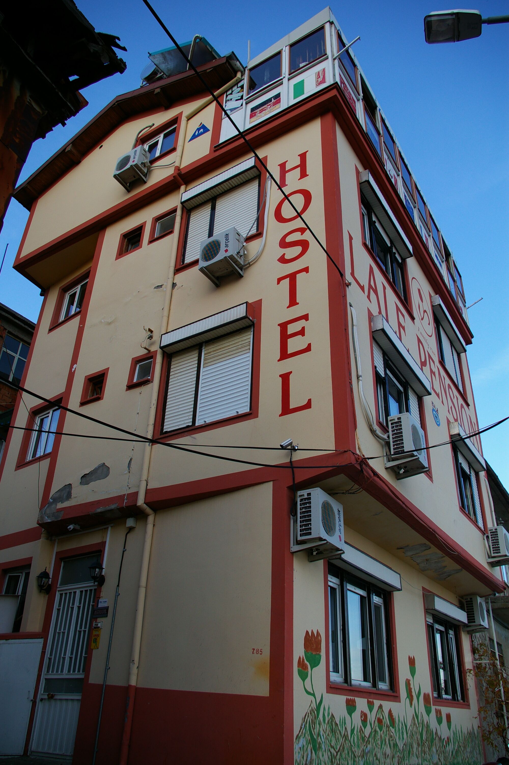 A hostel building with multiple floors, air conditioning units, and a sign indicating it is a hostel.