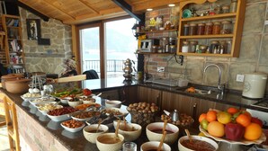 A kitchen with a stone wall, wooden shelves, and a variety of food items and utensils. - Lale Pansiyon (Egirdir)