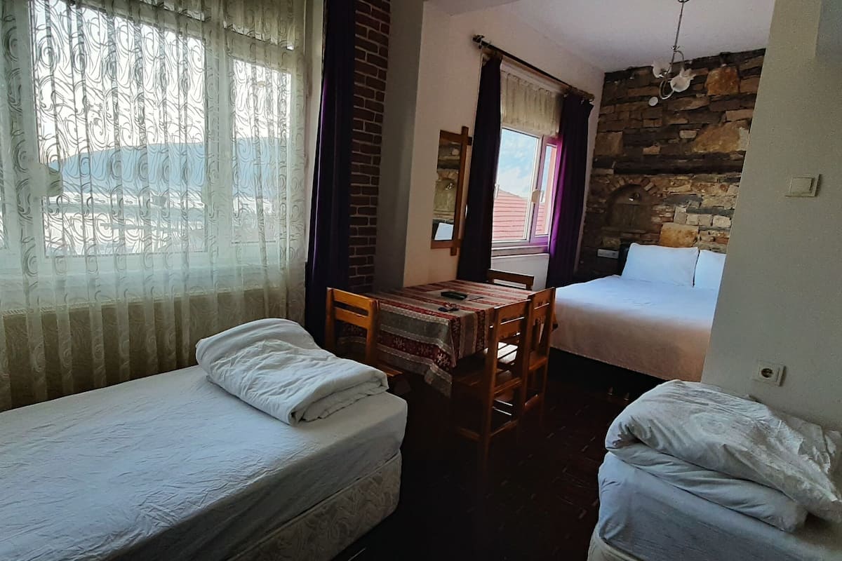 A room with two single beds, a wooden table, and a window with curtains.