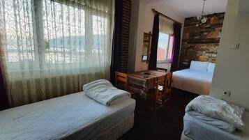 A room with two single beds, a wooden table, and a window with curtains.