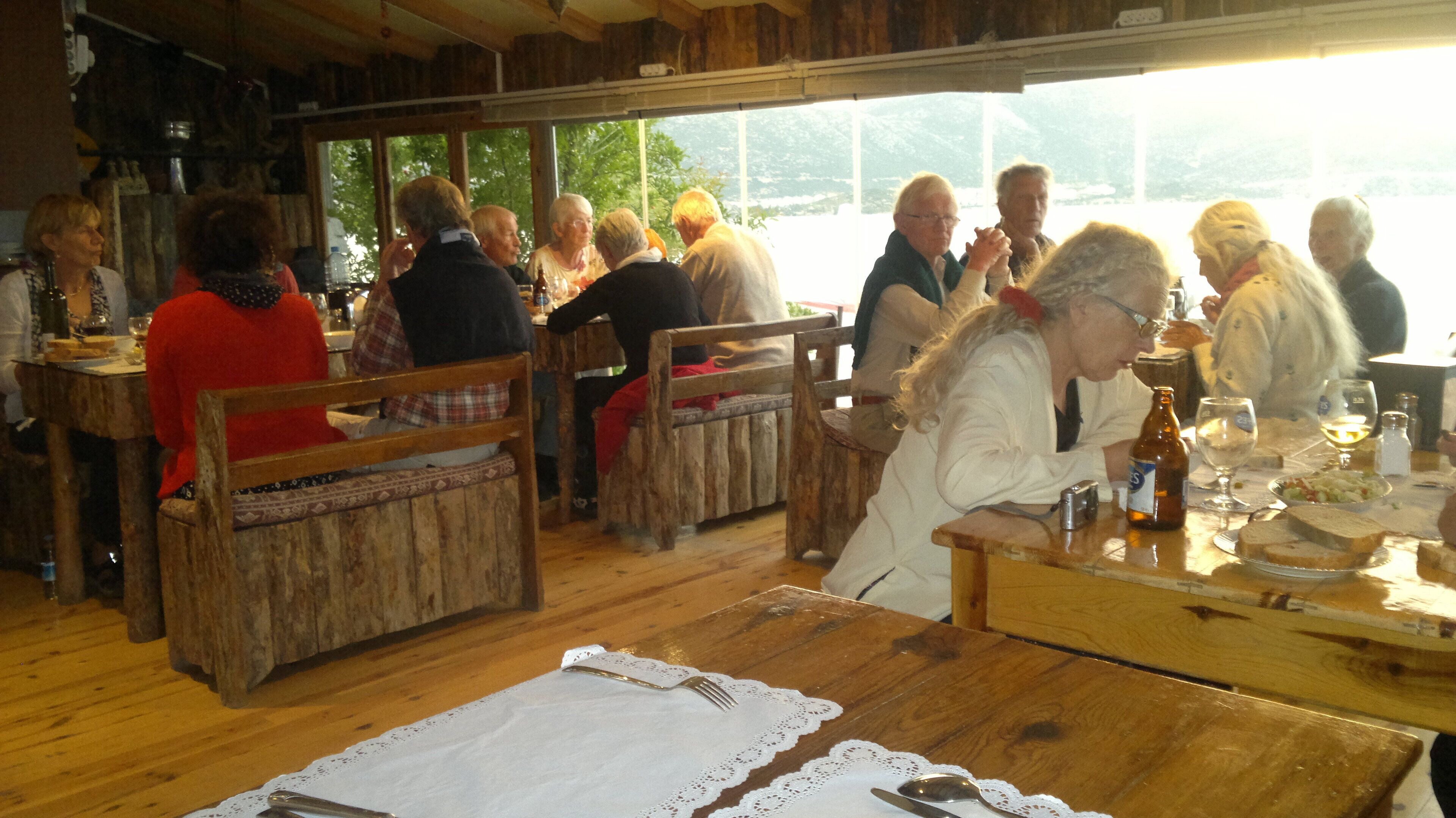 A rustic wooden interior with wooden benches and tables, a view of greenery outside, and a casual dining atmosphere.