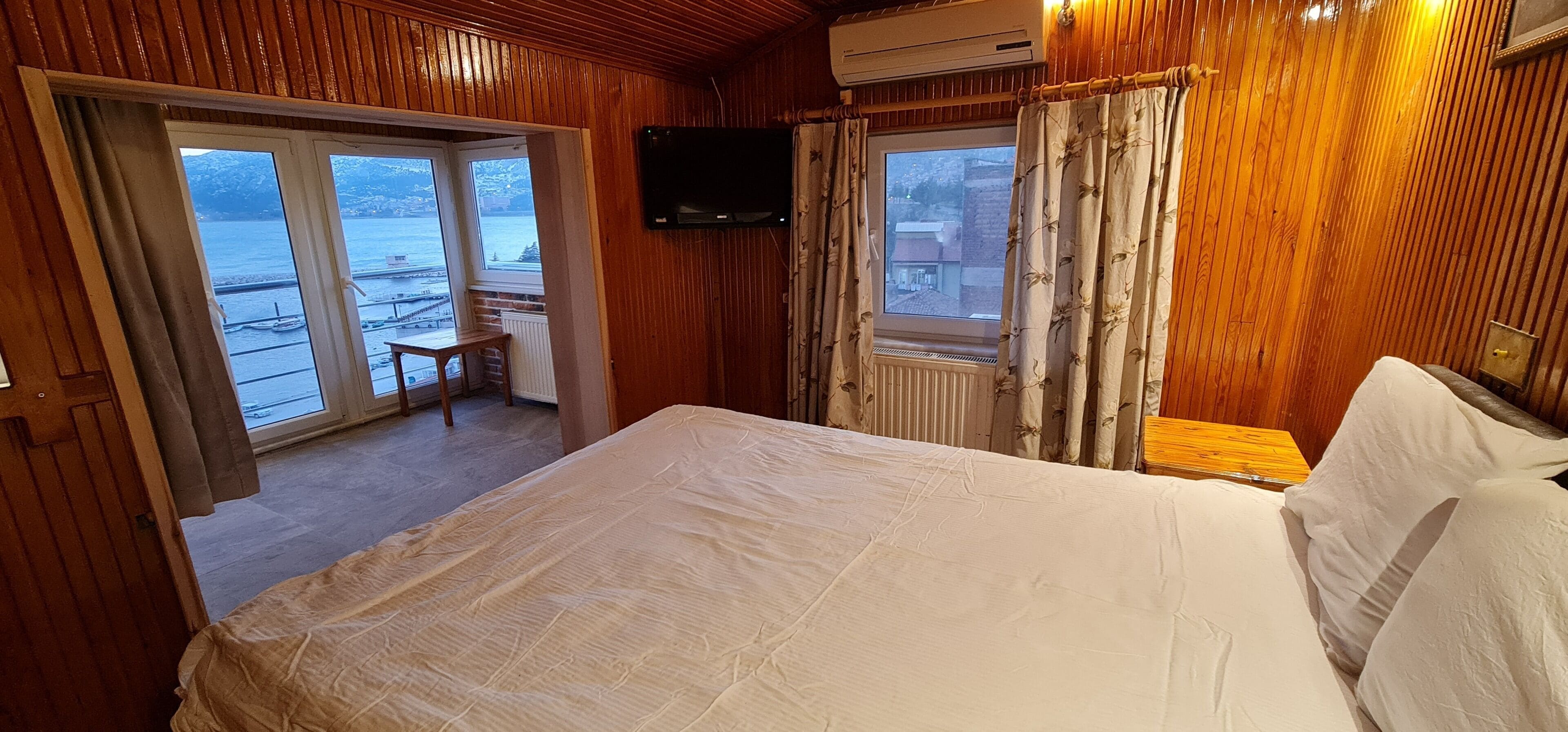 Ein Zimmer mit Holzwänden, einem Bett, einem an der Wand montierten Fernseher und Meerblick durch ein Fenster.
