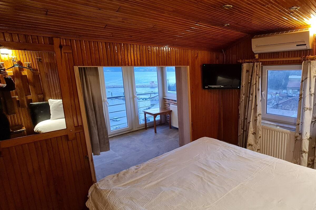 A wooden cabin room with a bed, a television, and a window with curtains.