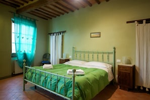 A bedroom with a metal bed frame, green bedding, a wooden nightstand, and a window with a curtain. - Il Rifugio d'Altri Tempi (Montalcino)