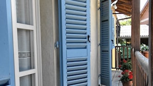 A wooden porch with blue shutters, potted plants, and a view of the street. - Agriturismo Cascina Ponchietta (Monta)