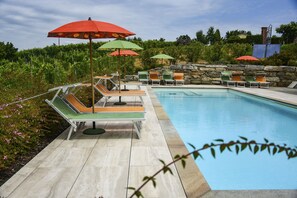 A pool area with lounge chairs and umbrellas, surrounded by a stone wall and greenery. - Agriturismo Cascina Ponchietta (Monta)