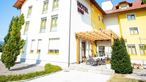 A hotel with a white facade and yellow accents, featuring a covered outdoor seating area. - Hotel Bau (Maribor)