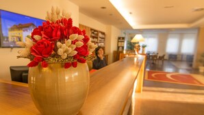A reception area with a vase of red and white flowers on a wooden counter. - Hotel Bau (Maribor)