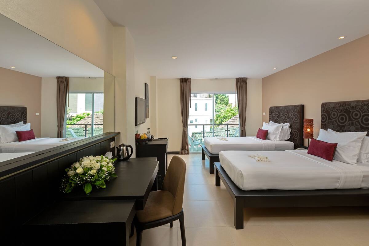 Une chambre d’hôtel équipée d’un bureau, de deux lits, d’un grand miroir et offrant une vue sur la verdure environnante.