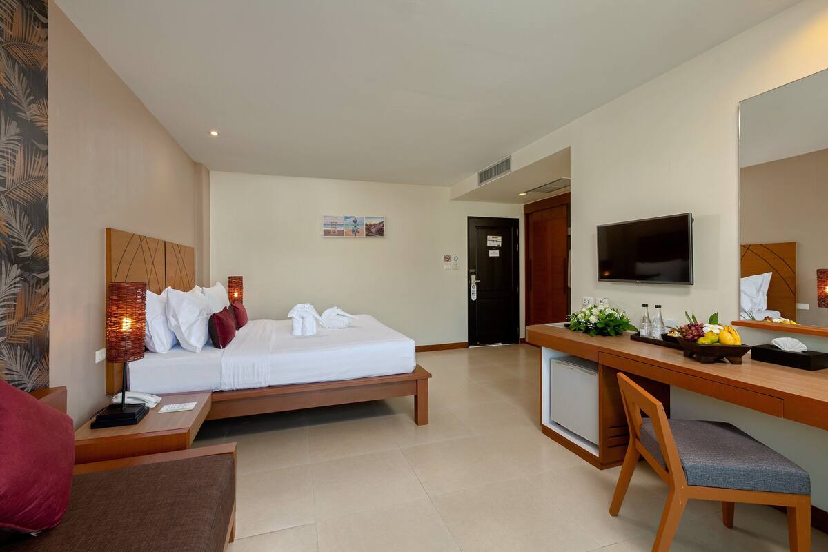 Une chambre d’hôtel comprenant un lit, une table de chevet, un bureau, une chaise, une télévision et une petite kitchenette.