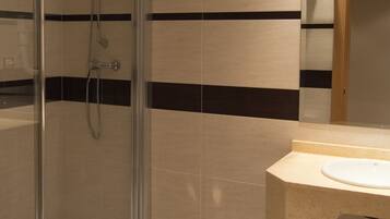 A bathroom with a glass-enclosed shower, a toilet, and a sink with a mirror above it.