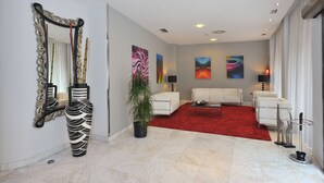 Una sala de estar moderna con alfombra roja, sofás blancos, una mesa de centro y arte abstracto en la pared.