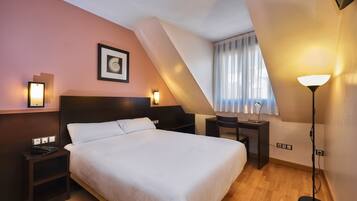 Una habitación de hotel con una cama grande, mesitas de noche, un escritorio y una lámpara.