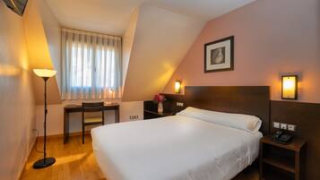 A hotel room with a large bed, a desk, a chair, a lamp, and a nightstand with a phone.