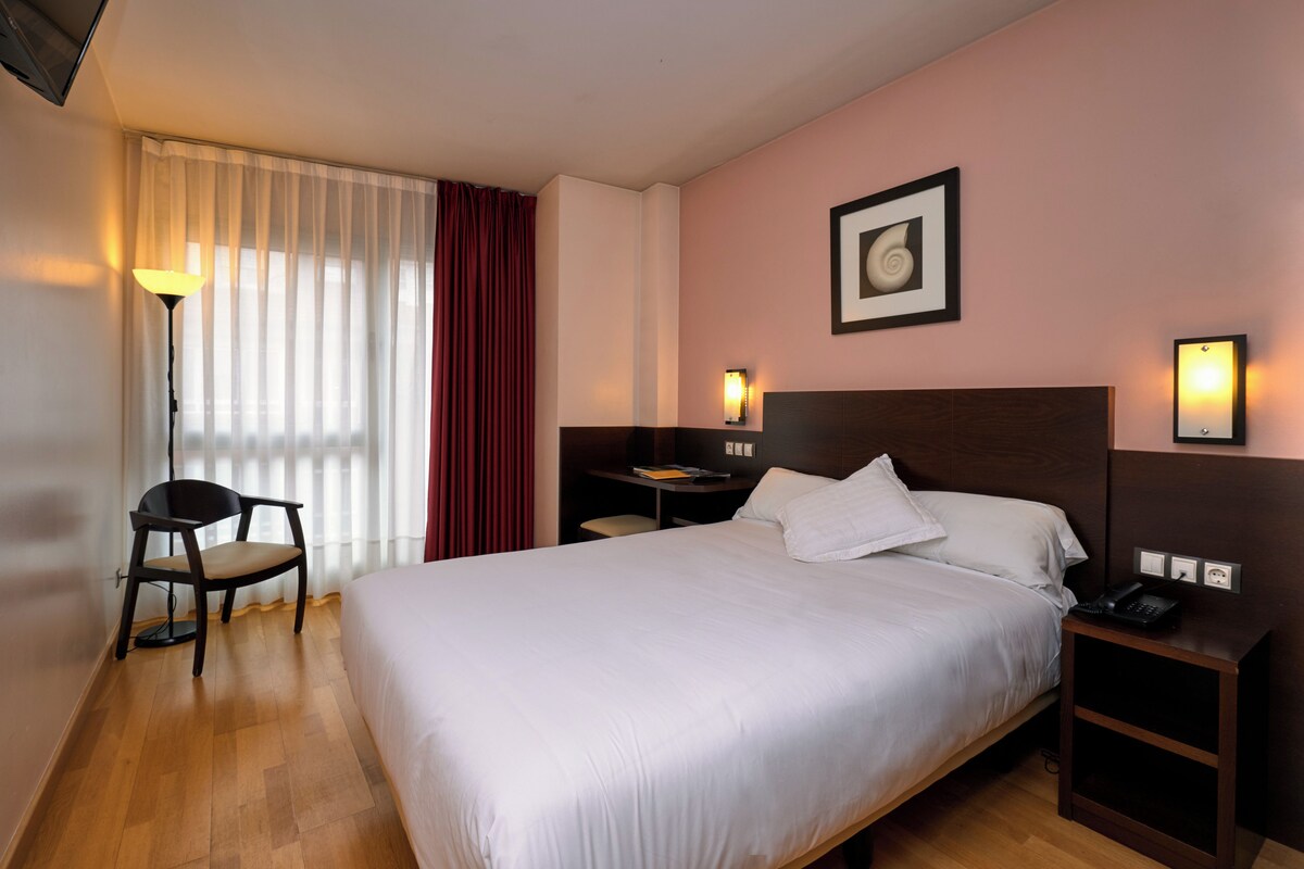 Ein Hotelzimmer mit einem großen Bett, einem Schreibtisch, einem Stuhl, einer Lampe und einem Bild an der Wand.