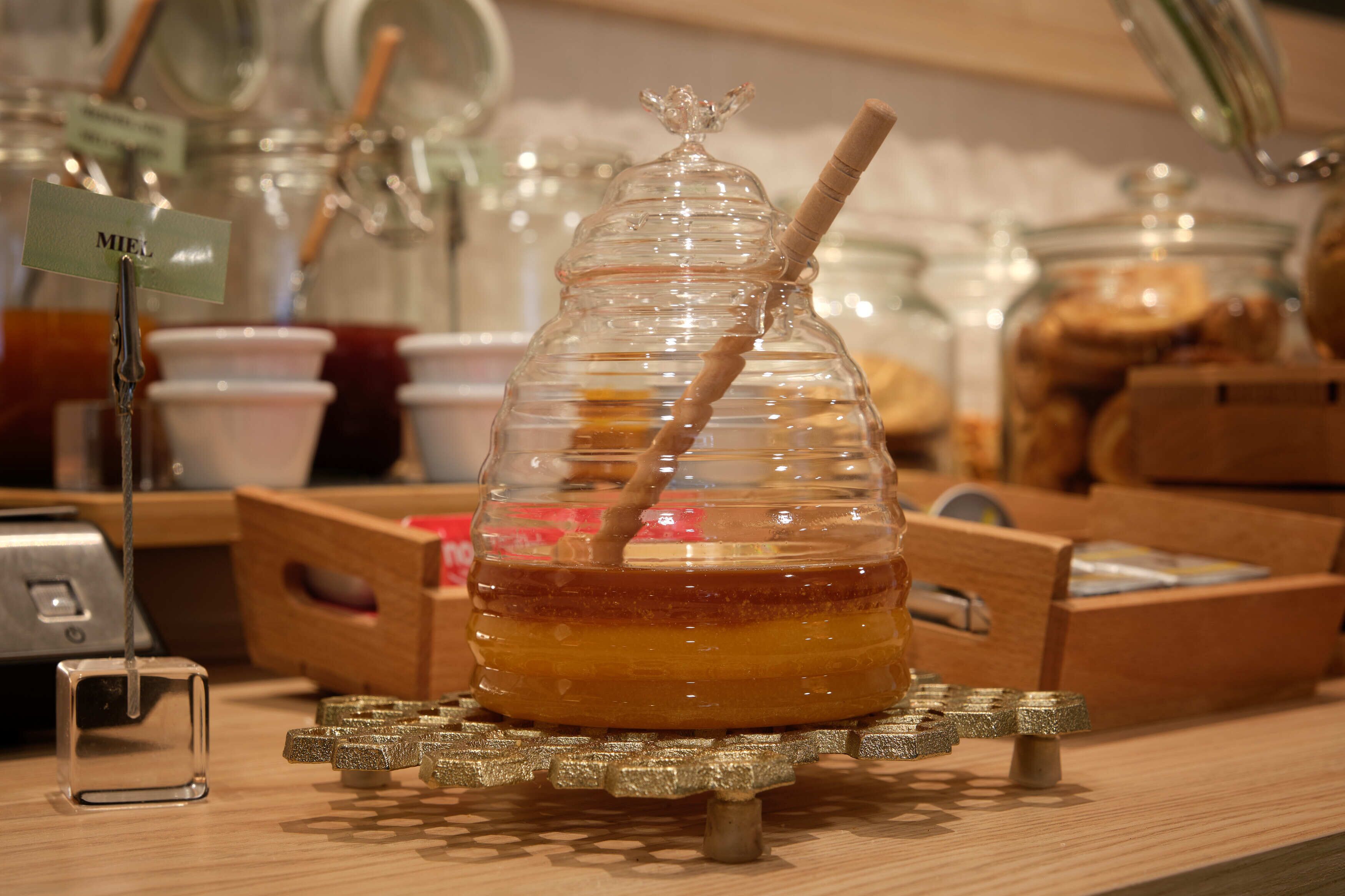 Un tarro de miel con una ramita de madera, sobre un pedestal de madera.