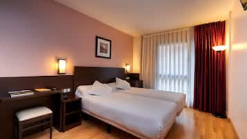 Habitació d'hotel amb dos llits, una escriptori, una cadira, una taula de nit i una làmpada.