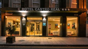 Hotel Castro Real con fachada de vidrio, un letrero con estrellas y una bandera estadounidense en el interior.