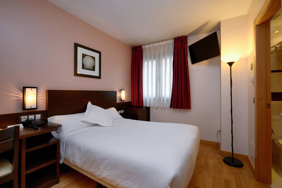A hotel room with a large bed, bedside tables, a flat-screen TV, a standing lamp, and a framed picture on the wall.