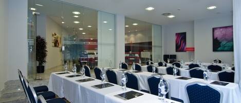 Un salón de conferencias con mesas dispuestas para una reunión, equipado con sillas y vasos de agua.