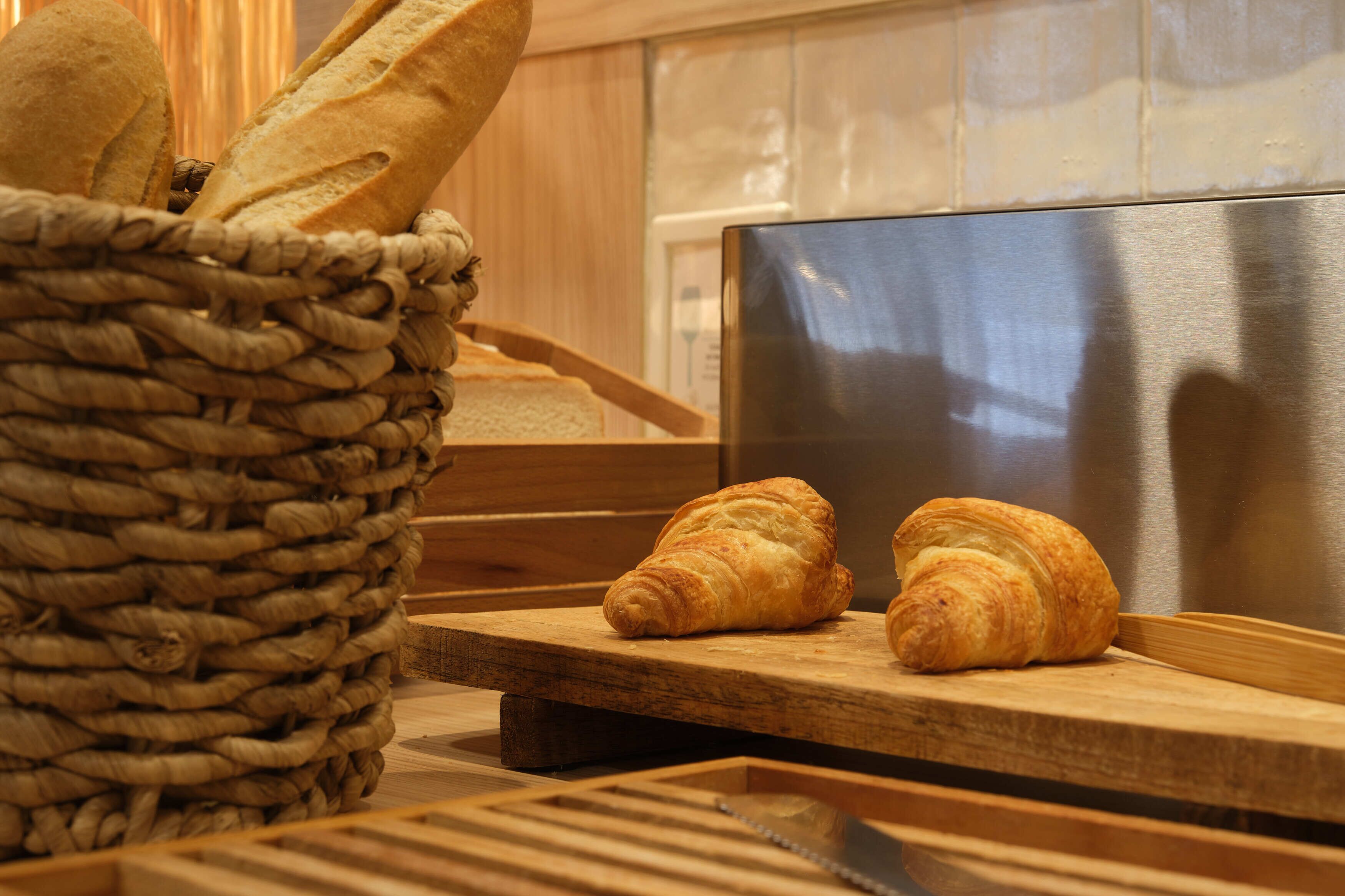 A basket of baguettes and croissants on a wooden counter in a bakery setting.